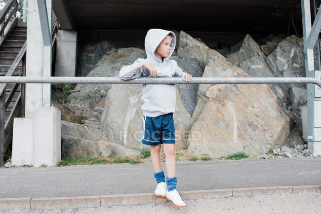 Menino de pé contra um poste olhando para a pista em roupas esportivas — Fotografia de Stock