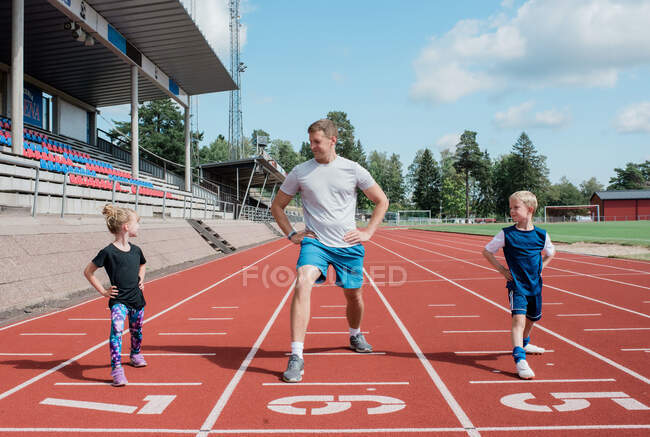 Father doing stretches with his kids on a race track — Stock Photo