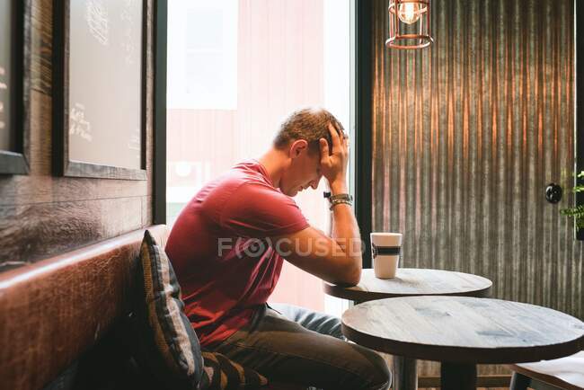 Man sat feeling stressed with his face in his hands in a cafe — Stock Photo