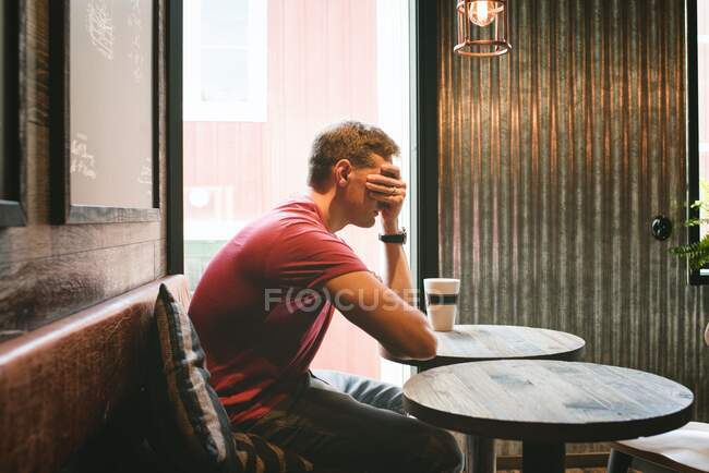 Man sat covering his face feeling stressed whilst sat in a cafe — Stock Photo