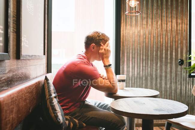 Homem sentado cobrindo seu rosto olhando estressado enquanto em um café bebendo — Fotografia de Stock