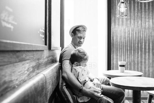 Father sat cuddling his son whilst drinking coffee in a cafe — Stock Photo