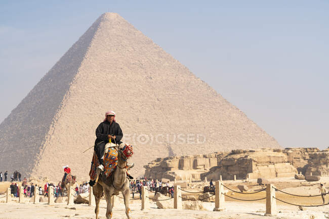 Ein Mann reitet mit einer Menschenmenge hinter sich von der Pyramide von Gizeh weg — Stockfoto