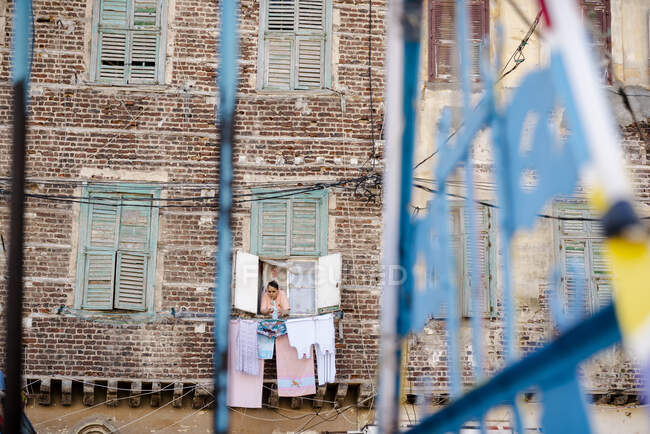 Une femme accroche une blanchisserie à la fenêtre de son appartement à Alexandrie, en Égypte — Photo de stock