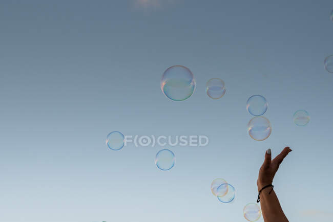 Una mano intenta tocar burbujas en el cielo - foto de stock