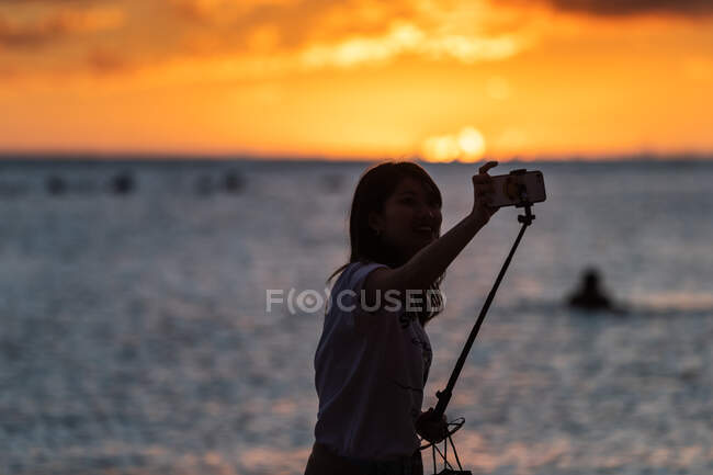 Mulher tira selfie na frente do oceano ao pôr do sol — Fotografia de Stock