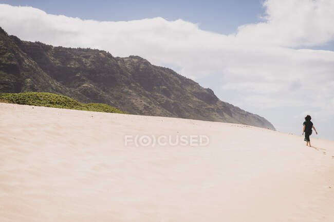 Woman walks up sandy hill towards mountains in Hawaii — Stock Photo