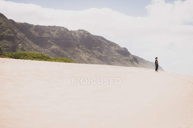 Woman stands on a sandy hill in the distance in front of the mountains — Stock Photo