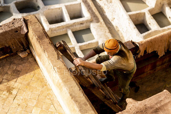 Hombre marroquí escalando escalera en curtiduría Fez - foto de stock