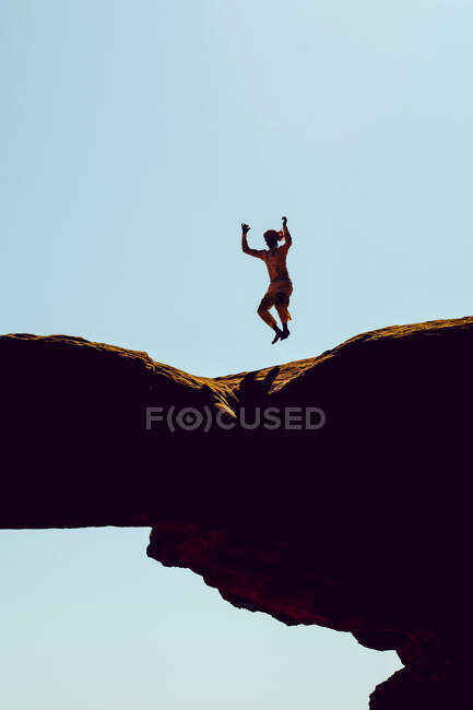 Un hombre beduino salta sobre un arco de roca en Wadi Rum, Jordania - foto de stock