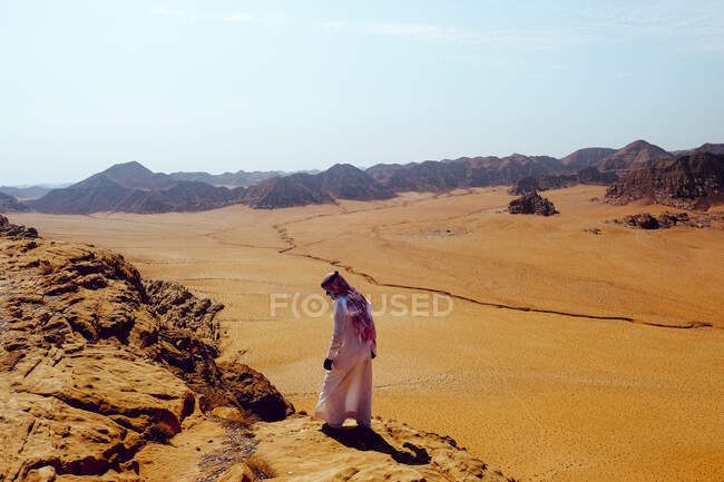 Hombre beduino camina por un acantilado con vistas a Wadi Rum, Jordania - foto de stock
