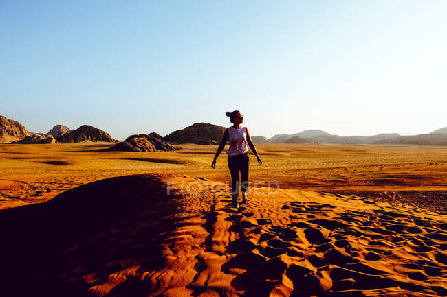 Una mujer camina por una duna de arena en Wadi Rum, Jordania al atardecer - foto de stock