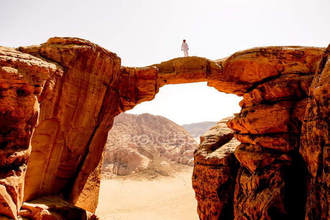 Un hombre beduino se levanta sobre un arco de roca en Wadi Rum, Jordania - foto de stock