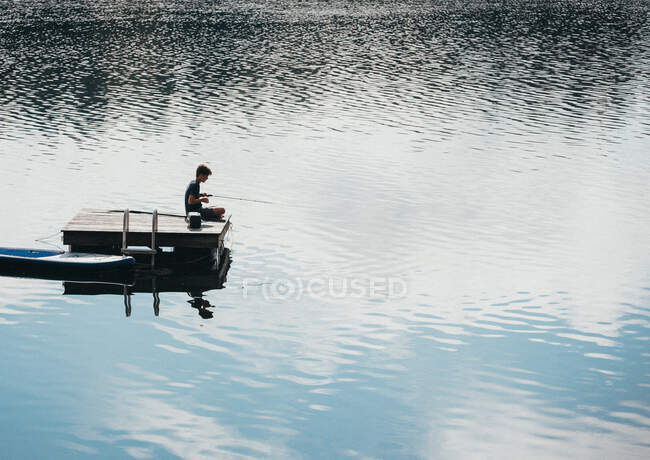 Adolescente niño pescando desde una plataforma de baño en un lago en el verano. - foto de stock