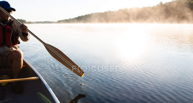 Hombre remando en canoa por la mañana en un lago brumoso en Ontario, Canadá. - foto de stock
