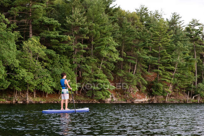 Adolescente niño remando en un SUP en el lago en Ontario, Canadá en un día soleado. - foto de stock
