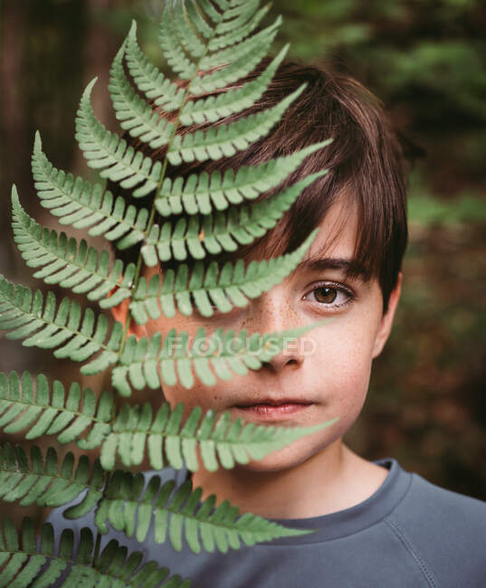 Retrato de menino cobrindo metade de seu rosto com uma folha de samambaia. — Fotografia de Stock