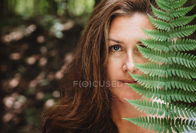 Portrait d'une femme brune couvrant la moitié de son visage avec une feuille de fougère. — Photo de stock