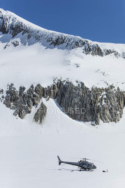 Helicopter parked on snow covered glacier below rocky mountain ridge. — Stock Photo
