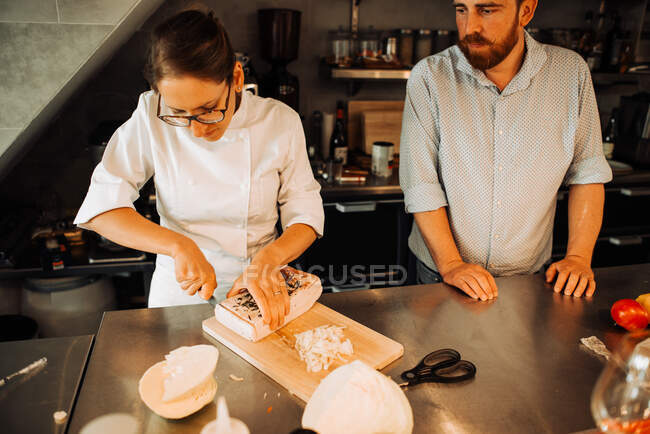 Female chef in uniform working at restaurant kitchen with assistant — Stock Photo