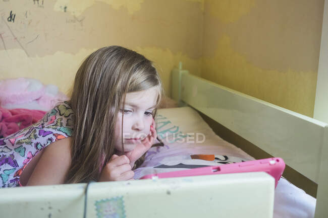 Молода дівчина лежить на її ліжку, дивлячись на її пристрій — стокове фото