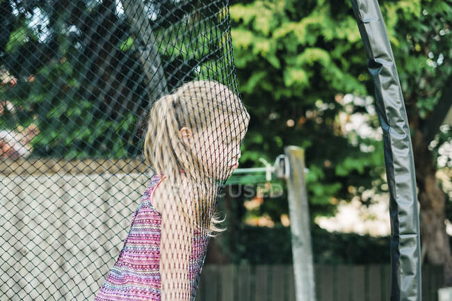 Young girl with grumpy face leaning on trampoline netting — Stock Photo