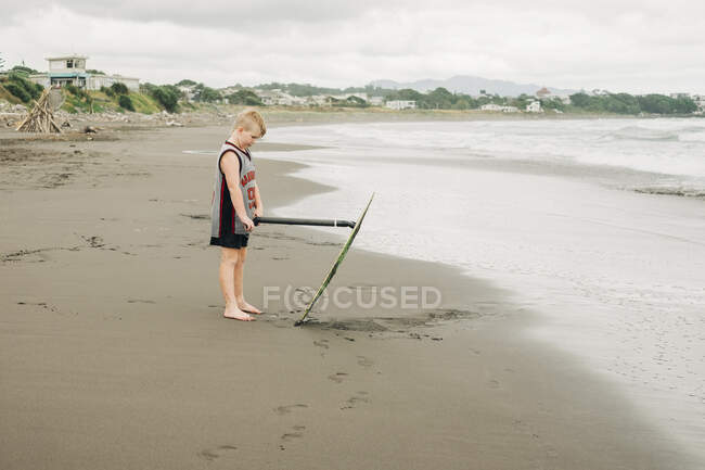 Joven niño de pie en la playa con su tabla de skim - foto de stock