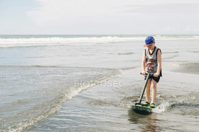 Мальчик играет на пляже в воде со своей доской — стоковое фото