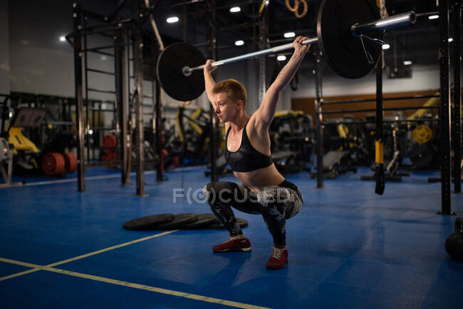 Сосредоточенный спортсмен приседает и поднимает штангу во время интенсивной тренировки в спортзале — стоковое фото