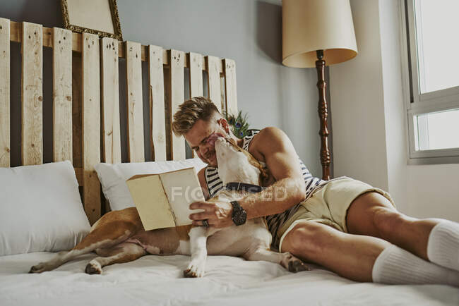 Un joven rubio leyendo en la cama con su perro. concepto de estilo de vida - foto de stock
