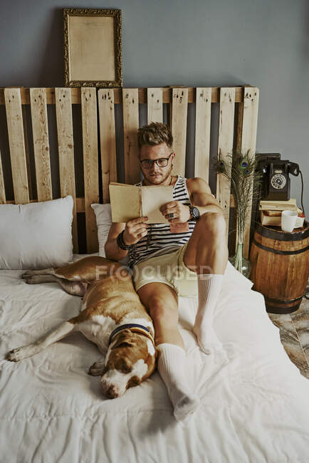 Ein kleiner blonder Junge liest im Bett mit seinem Hund. Lifestylekonzept — Stockfoto