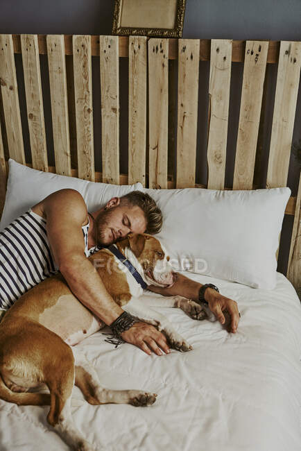 Un giovane ragazzo biondo che dorme accanto al suo cane nel letto. Stile di vita concetto — Foto stock