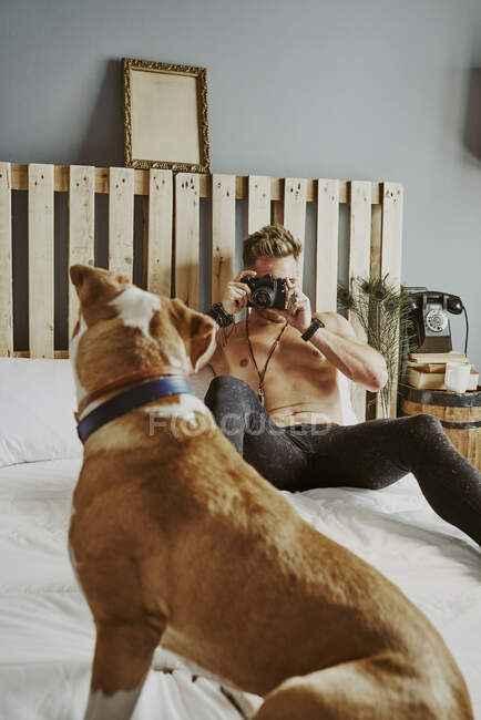 Un joven rubio tomando fotos de su perro en la cama. Concepto de estilo de vida - foto de stock