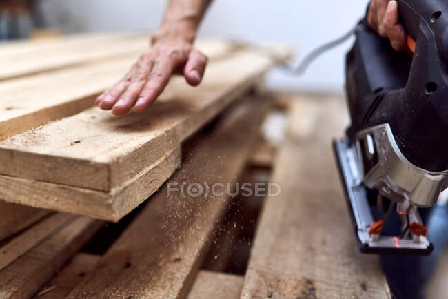 Hands of a young woman cutting wooden pallets with a jigsaw. concept of female empowerment — Stock Photo