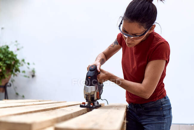 A young woman cutting wooden pallets with a jigsaw. concept of female empowerment — Stock Photo