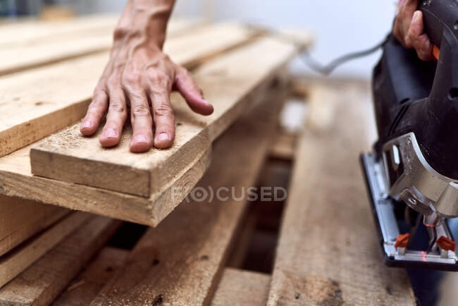 Hand of a young woman cutting wooden pallets with a jigsaw. concept of female empowerment — Stock Photo