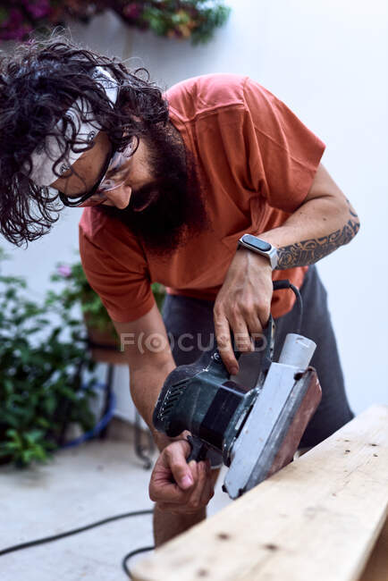 Jeune homme barbe polissage d'une planche de bois avec une ponceuse de puissance. concept de travail des femmes — Photo de stock