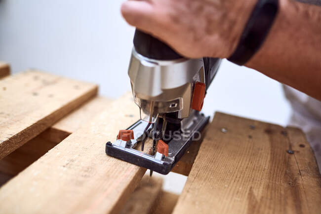 Hands of a young man cutting wooden pallets with a jigsaw. concept work of men — Stock Photo