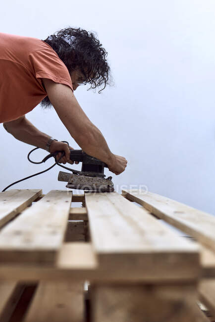 Junger Mann mit Bart poliert mit einem Elektroschleifer eine Holzplanke. Konzept der Frauenarbeit — Stockfoto