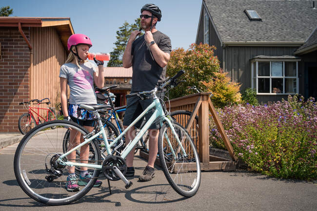 Padre e hija se ponen cascos de bicicleta y peparing para andar en bicicleta - foto de stock