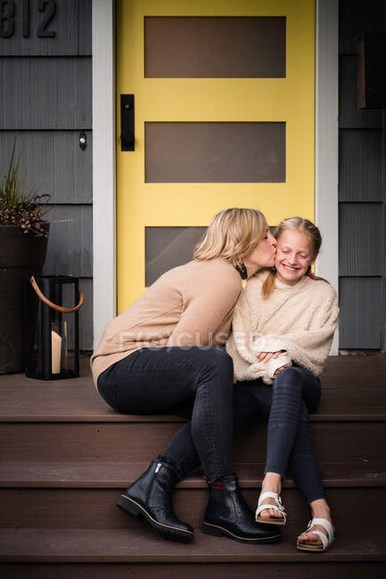 Mère embrassant sa fille sur les marches devant une porte jaune — Photo de stock