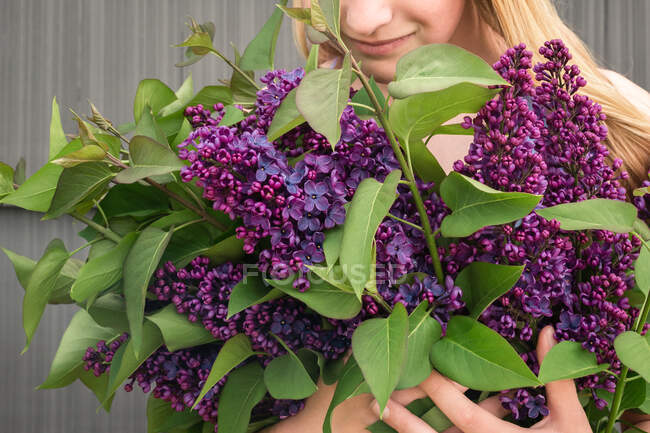Joven chica sosteniendo púrpura lila ramo mirando hacia abajo y sonriendo - foto de stock