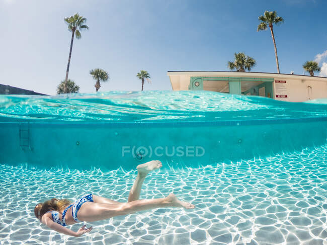 Ponto de vista de nível dividido da jovem garota nadando debaixo d 'água em uma piscina — Fotografia de Stock