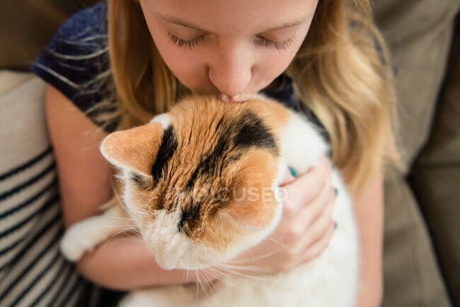 Primer plano de joven chica besos calico gato en casa - foto de stock