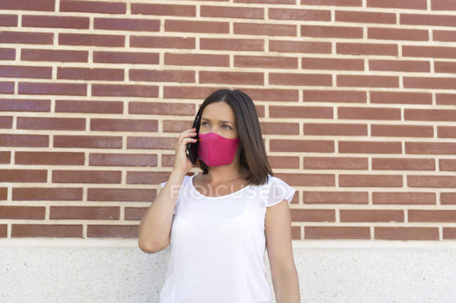 Mulher bonita com máscara falando em seu smartphone — Fotografia de Stock