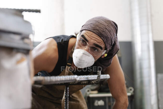 Чоловічий коваль в захисній масці в майстерні виконує металеві роботи — стокове фото