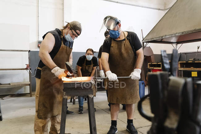 Blacksmiths forging metal detail while hitting hot iron with hammer — Stock Photo
