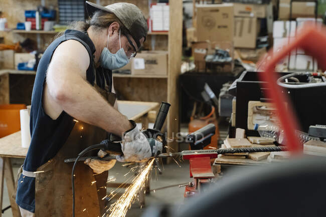Fleißiger Schmied schneidet während der Arbeit Metalldetails mit dem Schleifwerkzeug — Stockfoto