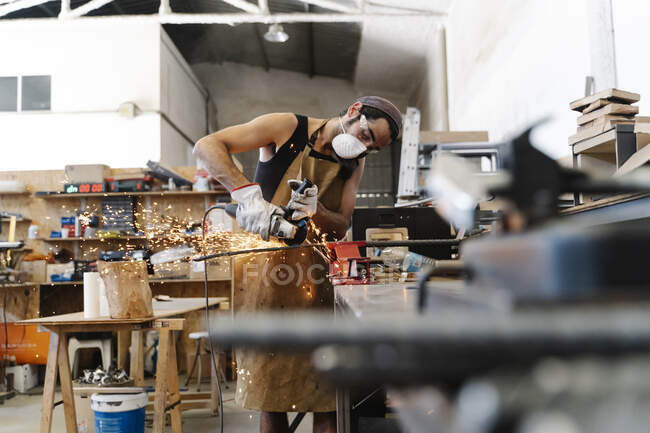 Busy blacksmith cutting metal detail with grinder tool while working — Stock Photo