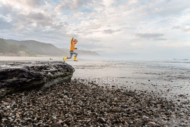 Young curly haired child leaping from a rock at the beach in New Zealand — Stock Photo